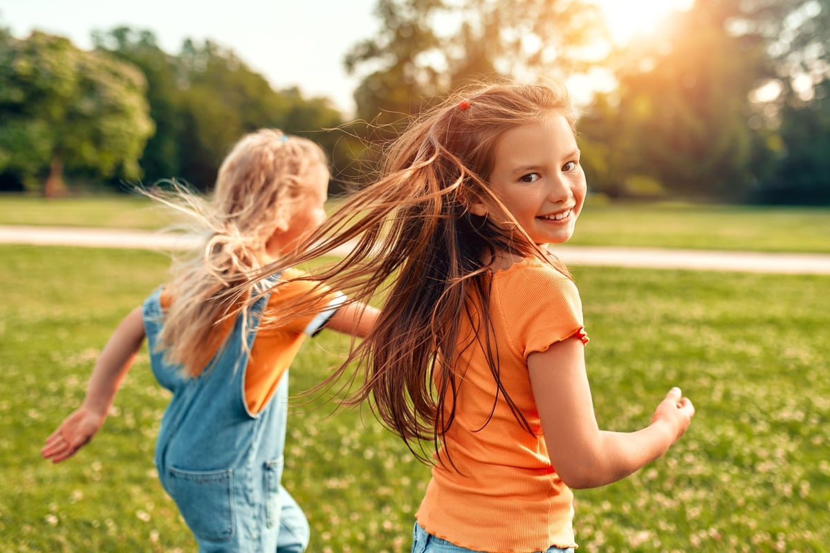Two little sisters running and playing together in a sunny meadow