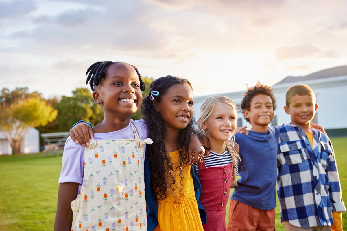 A group of diverse schoolchildren with arms around each other, smiling together