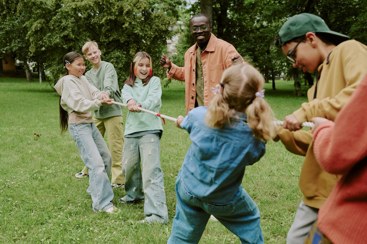 A group of multiethnic children pulling a rope together in a game of tug of war in a green park