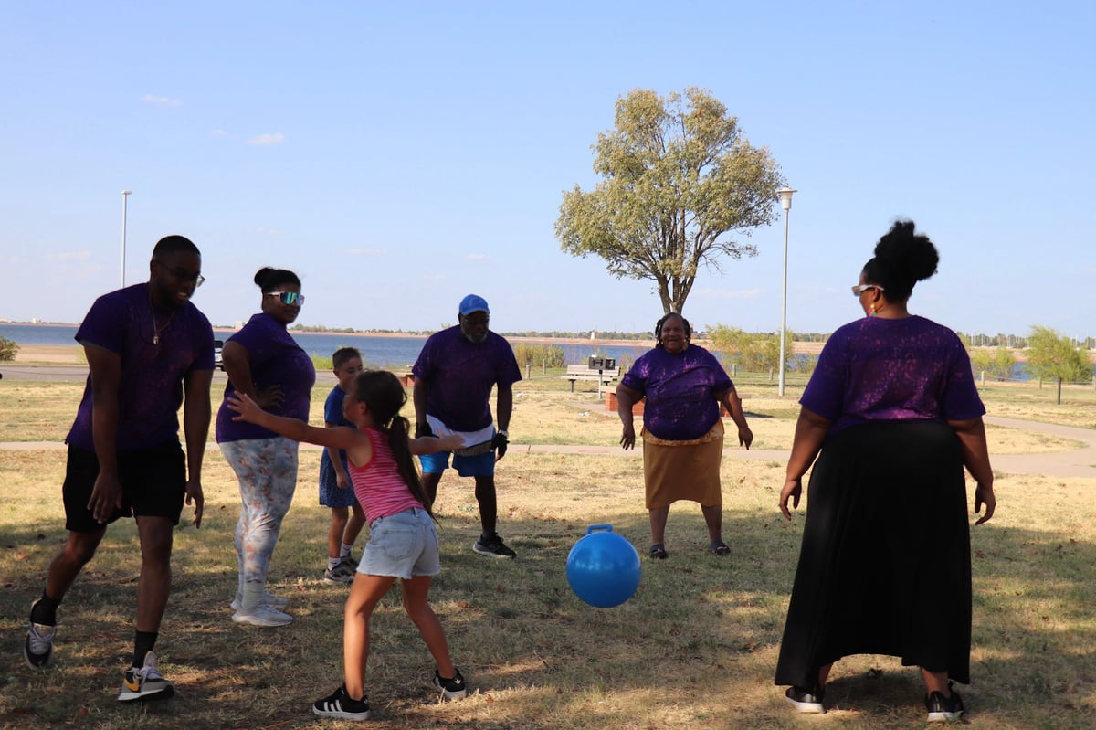 Group of people playing soccer in an open field on a sunny day with a tree and clear blue sky in the background