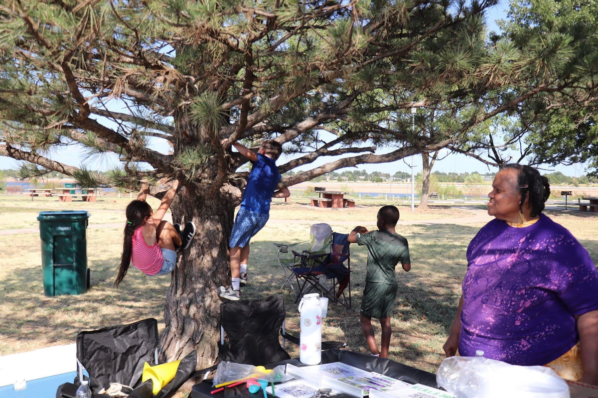Group of people gathered around a large tree at an outdoor community event in a field