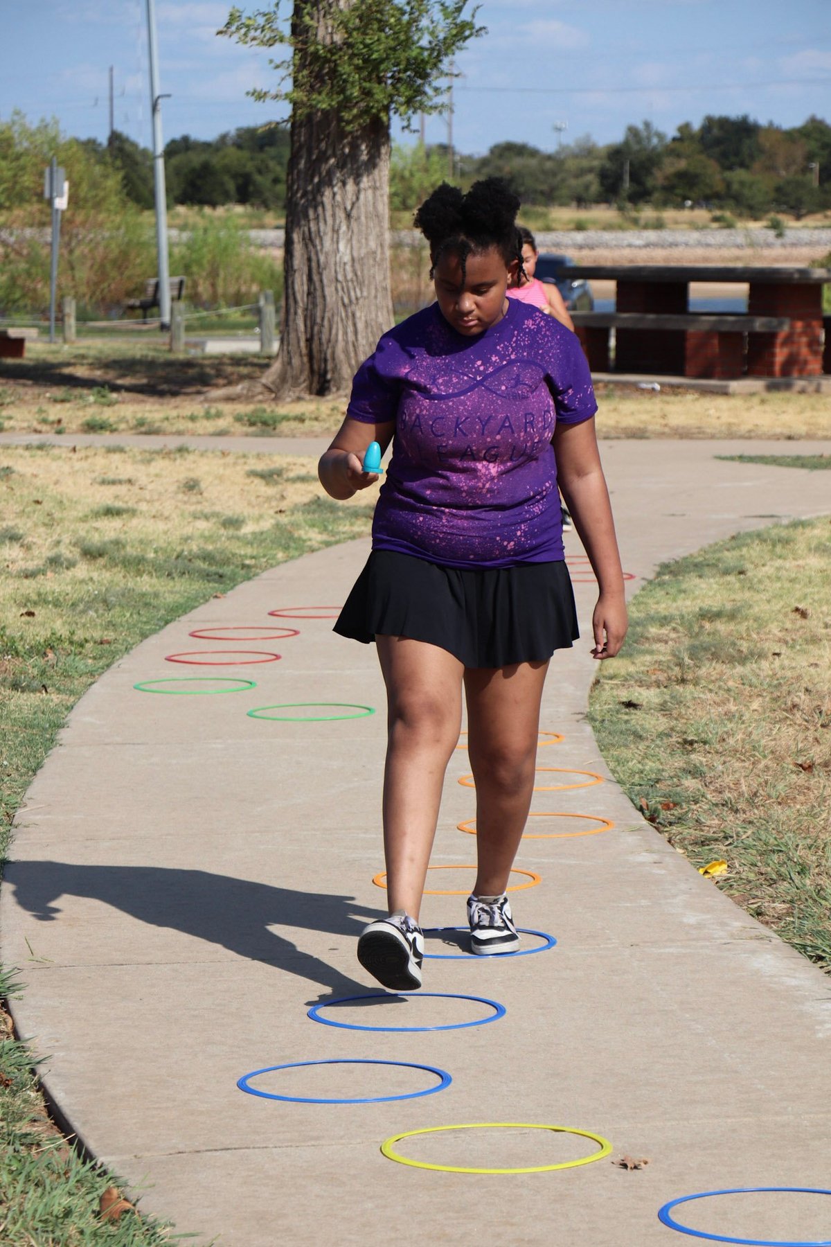 Woman in purple shirt doing agility training on a concrete path with colorful ring markers in a park