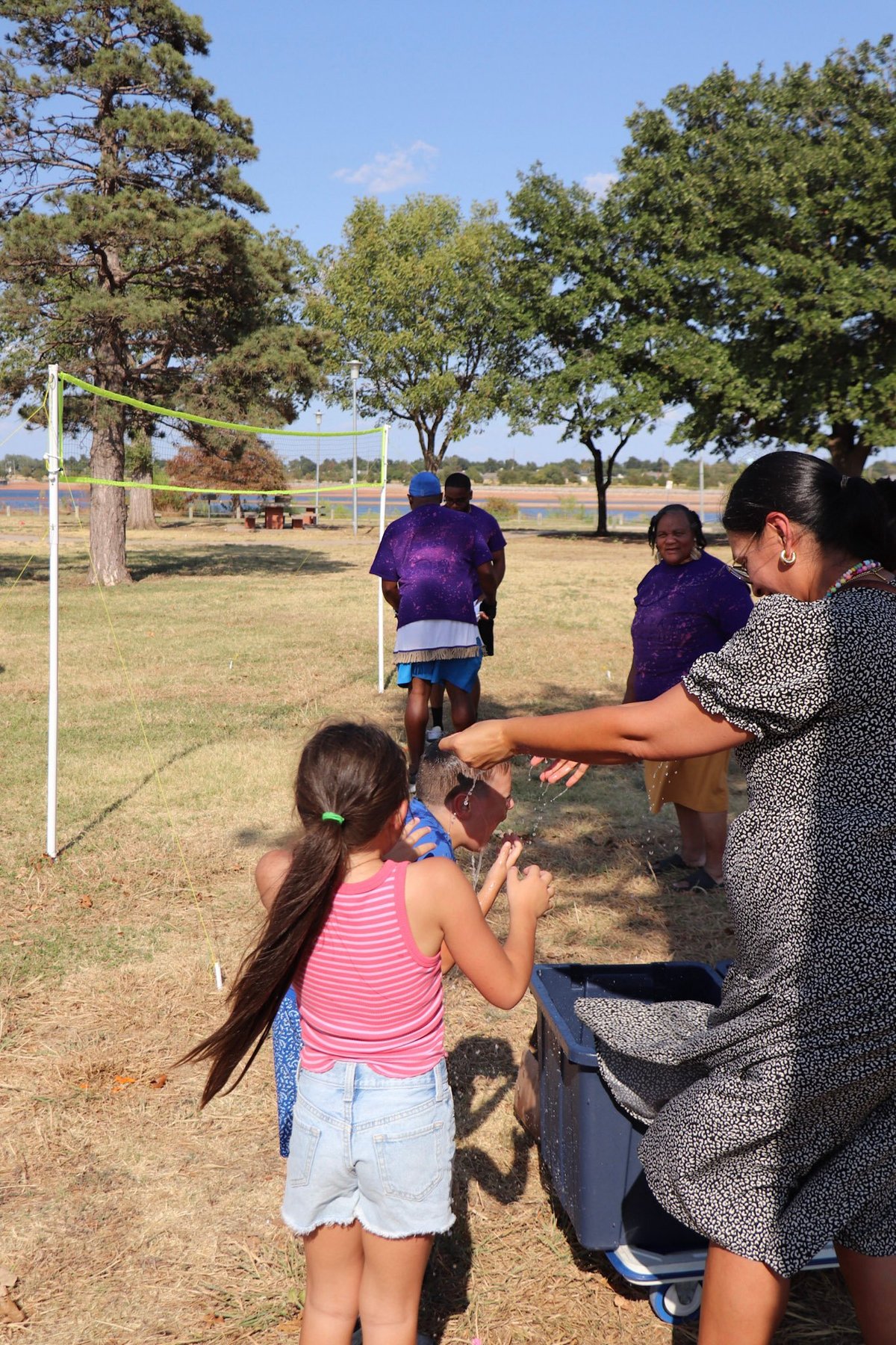 Adult teaching children volleyball outdoors in a park with trees and a net set up on the grass