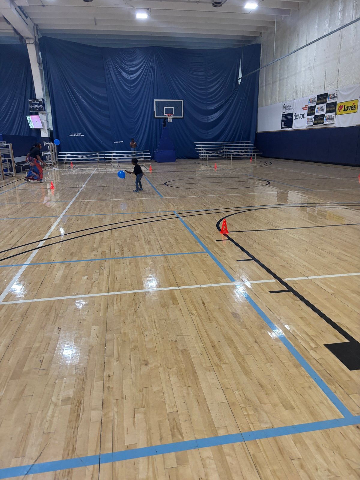 Children playing during a recreational activity session in an indoor gymnasium with a basketball hoop