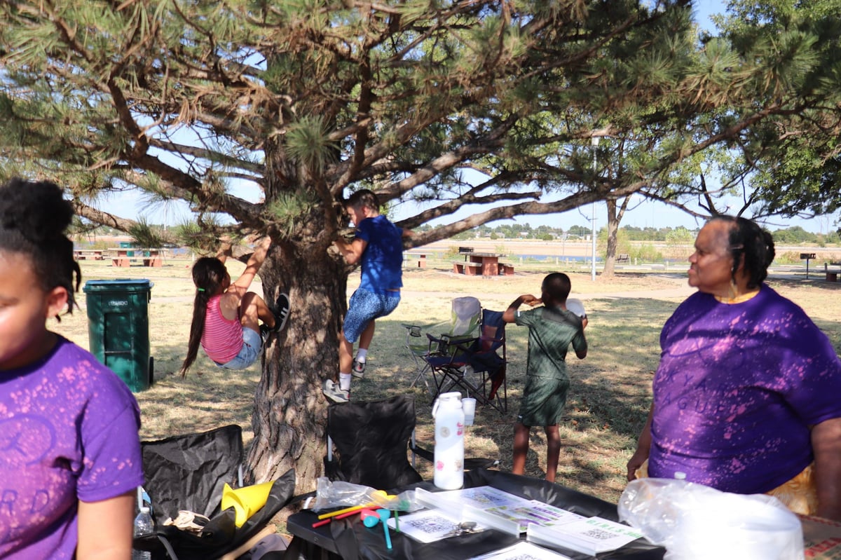 Group of people in purple shirts gathered under a large tree at an outdoor community event